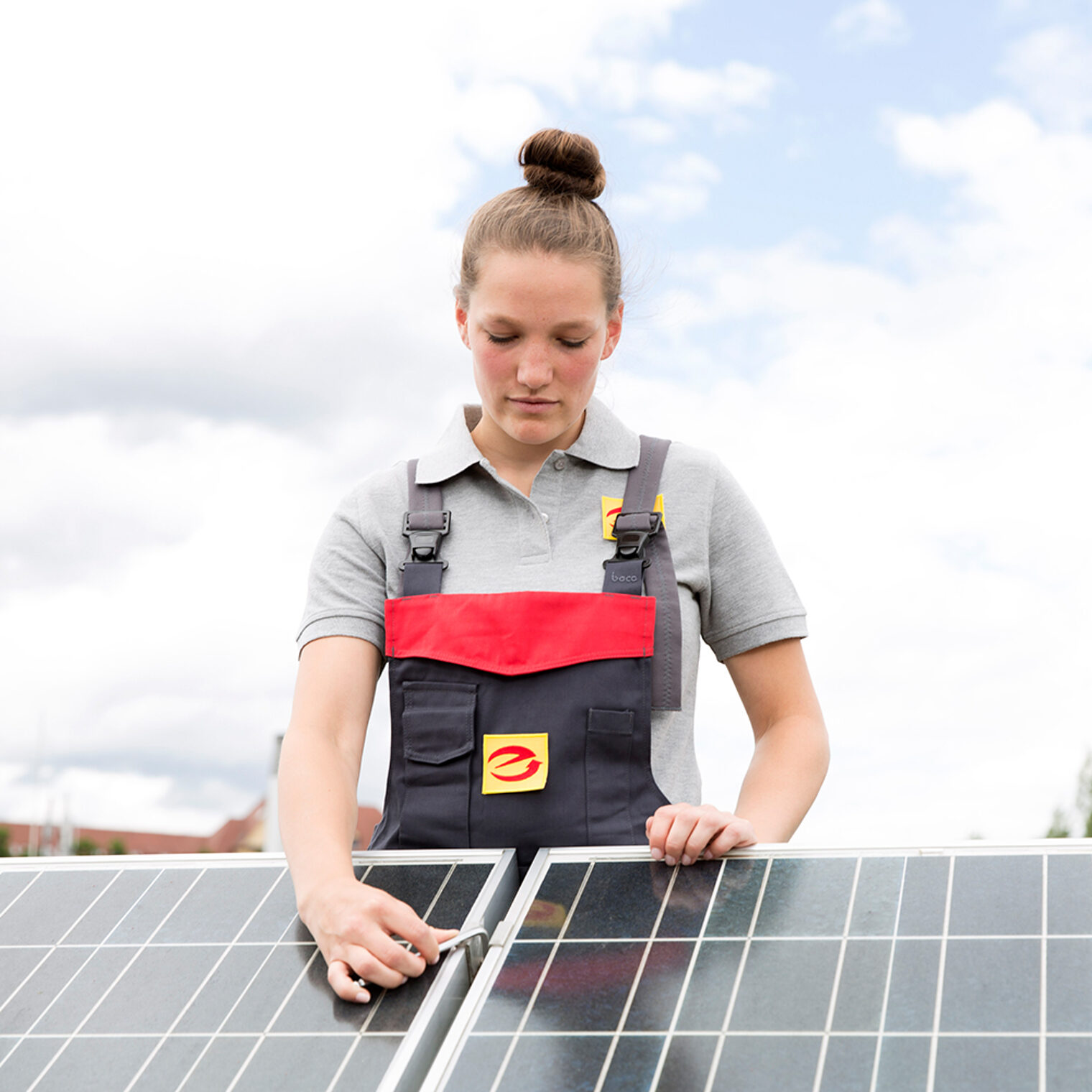 Junge Elektrotechnikerin auf einem Dach schraubt an einer Photovoltaik-Anlage.