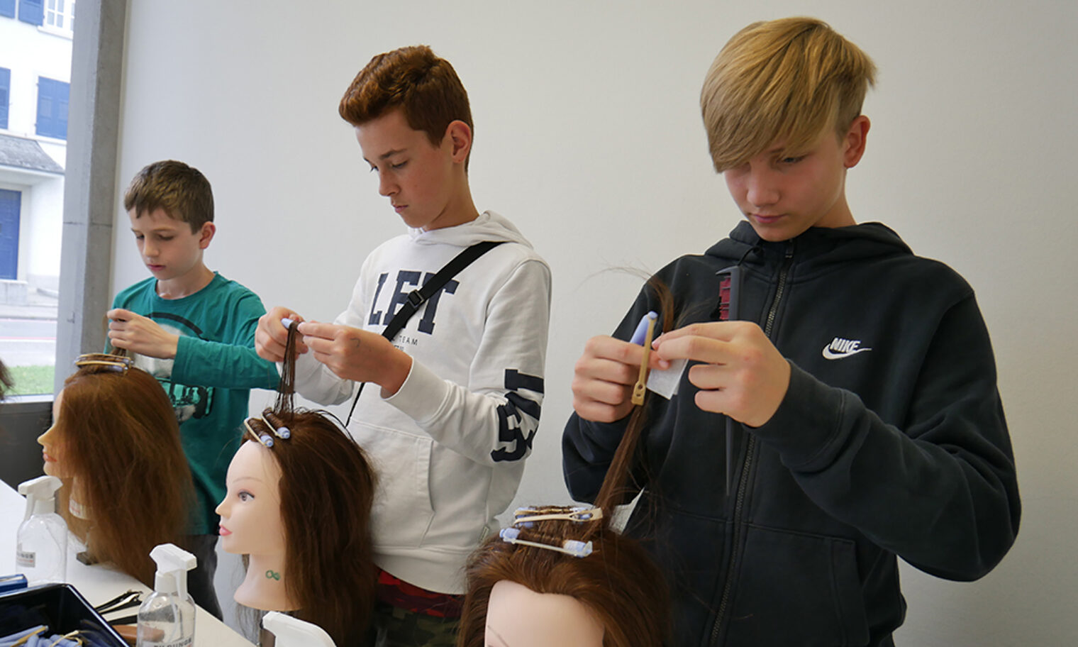 Drei Schüler frisieren Modellköpfe im Rahmen der Berufsorientierung an der Bildungsakademie Singen.