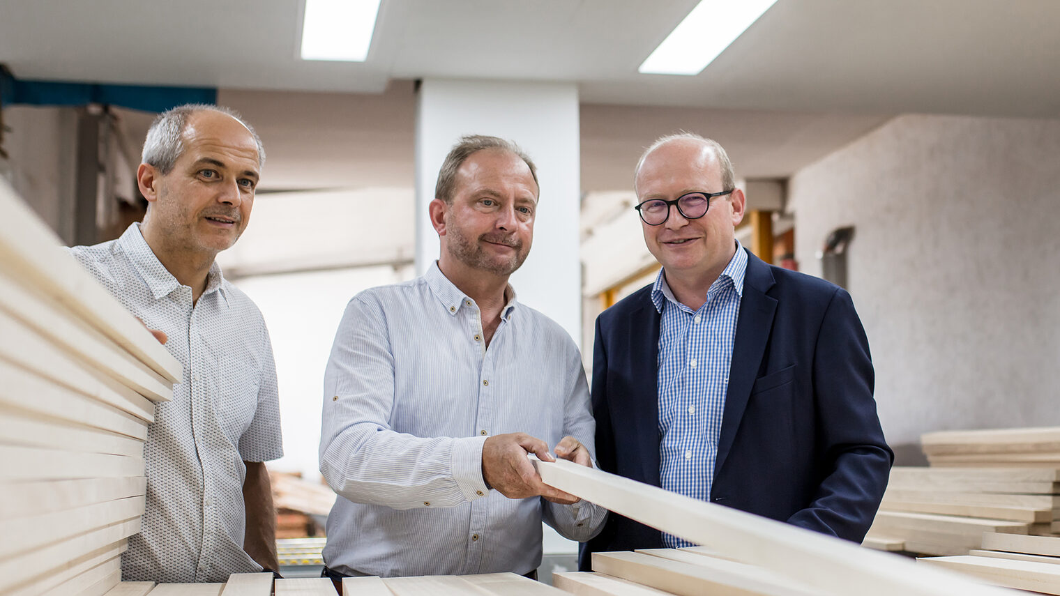 Die Brüder Bernd, Christian und Rainer Moser begutachten in ihrem Familienbetrieb Moser Massivholzplatten einen Stapel Holzleisten.