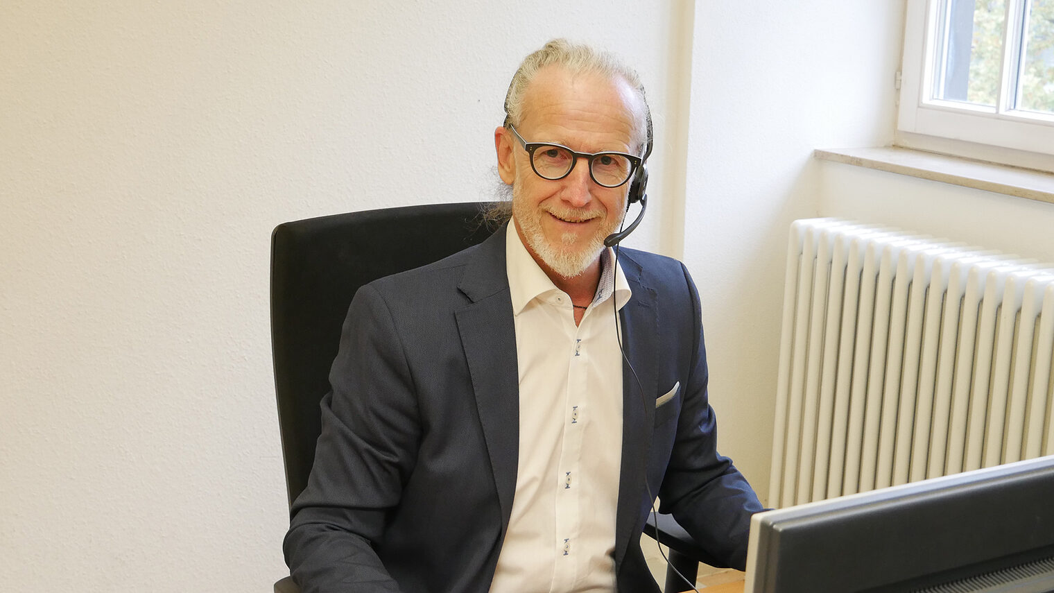 Thomas Thierolf, Dozent der Online-Akademie, sitzt mit Headset am Schreibtisch vor Computerbildschirm.
