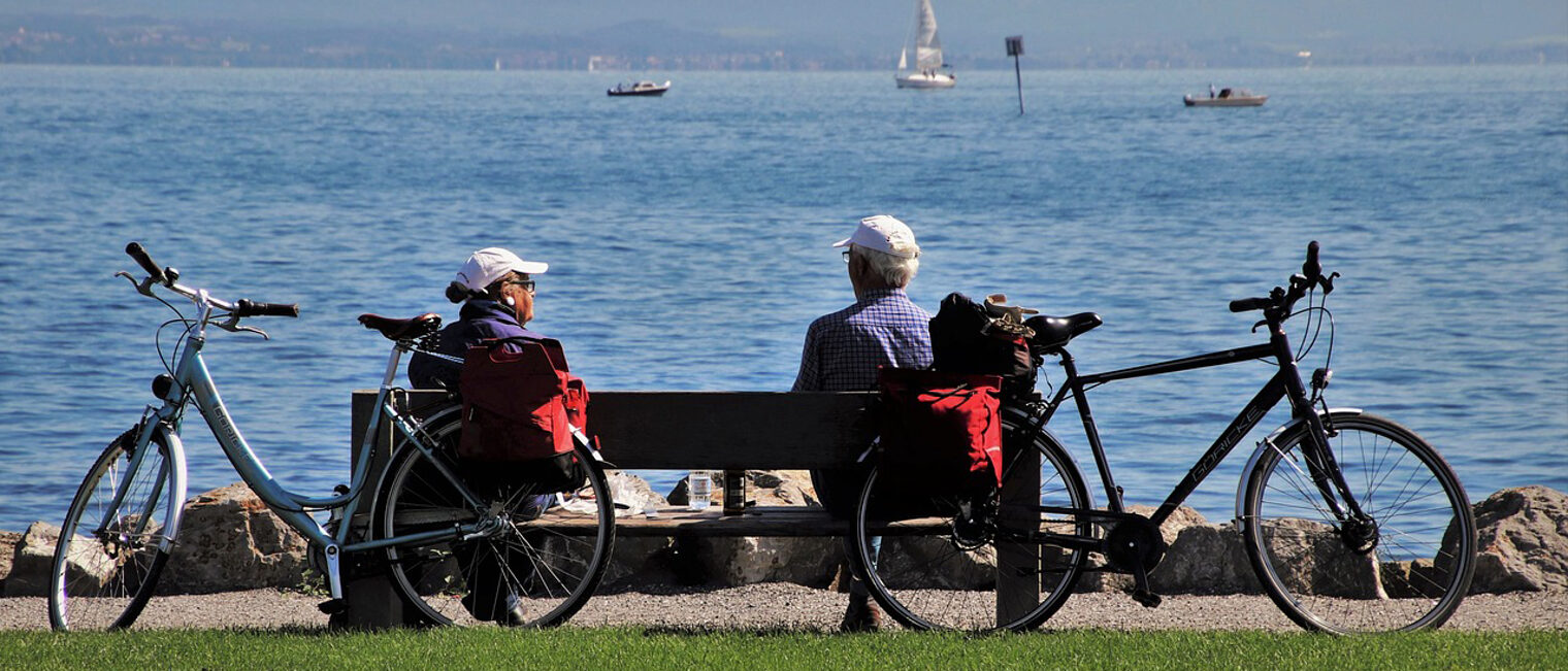 Ein Rentner-Ehepaar sitzt auf einer Bank am Bodensee.