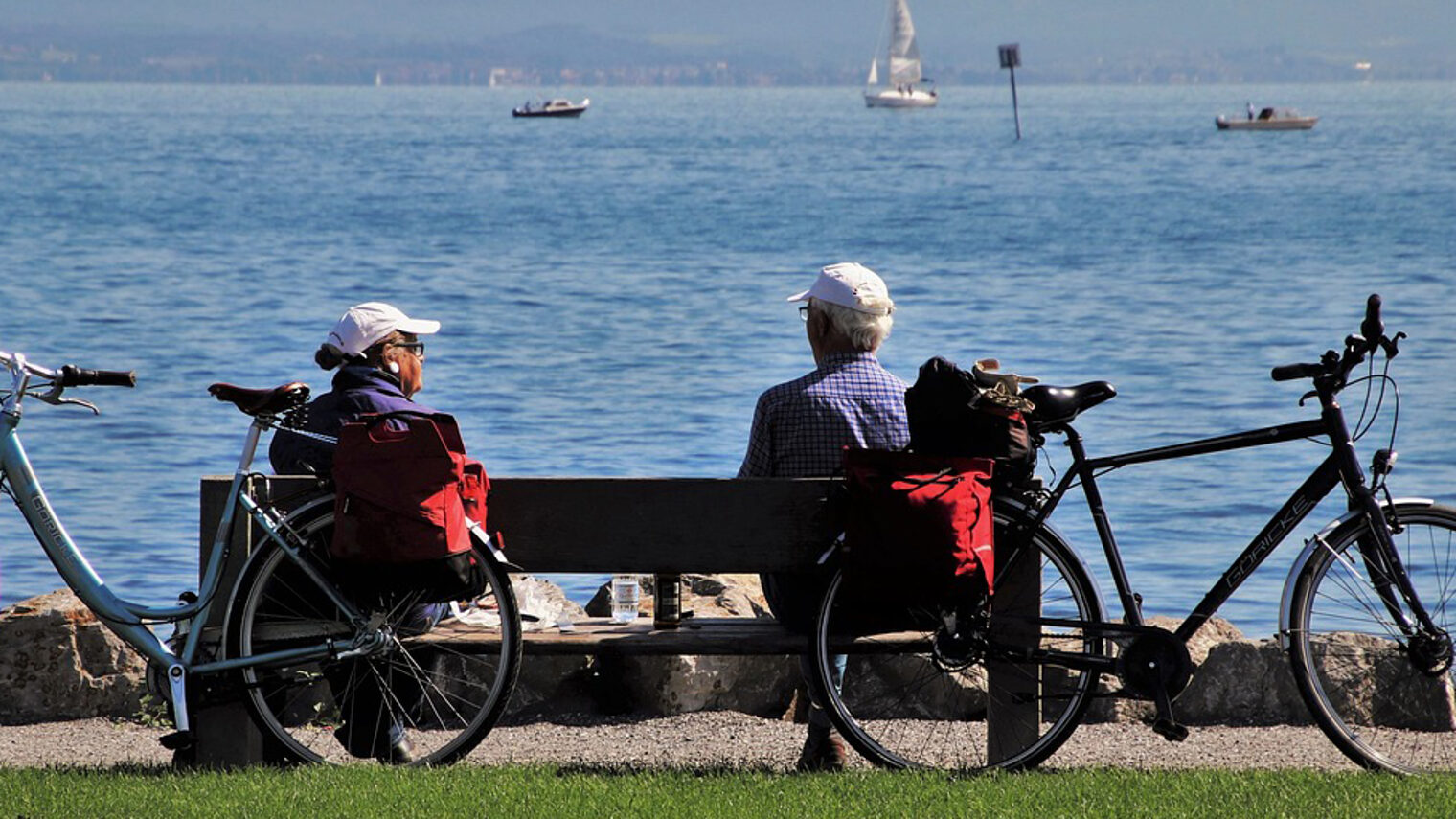 Ein Rentner-Ehepaar sitzt auf einer Bank am Bodensee.