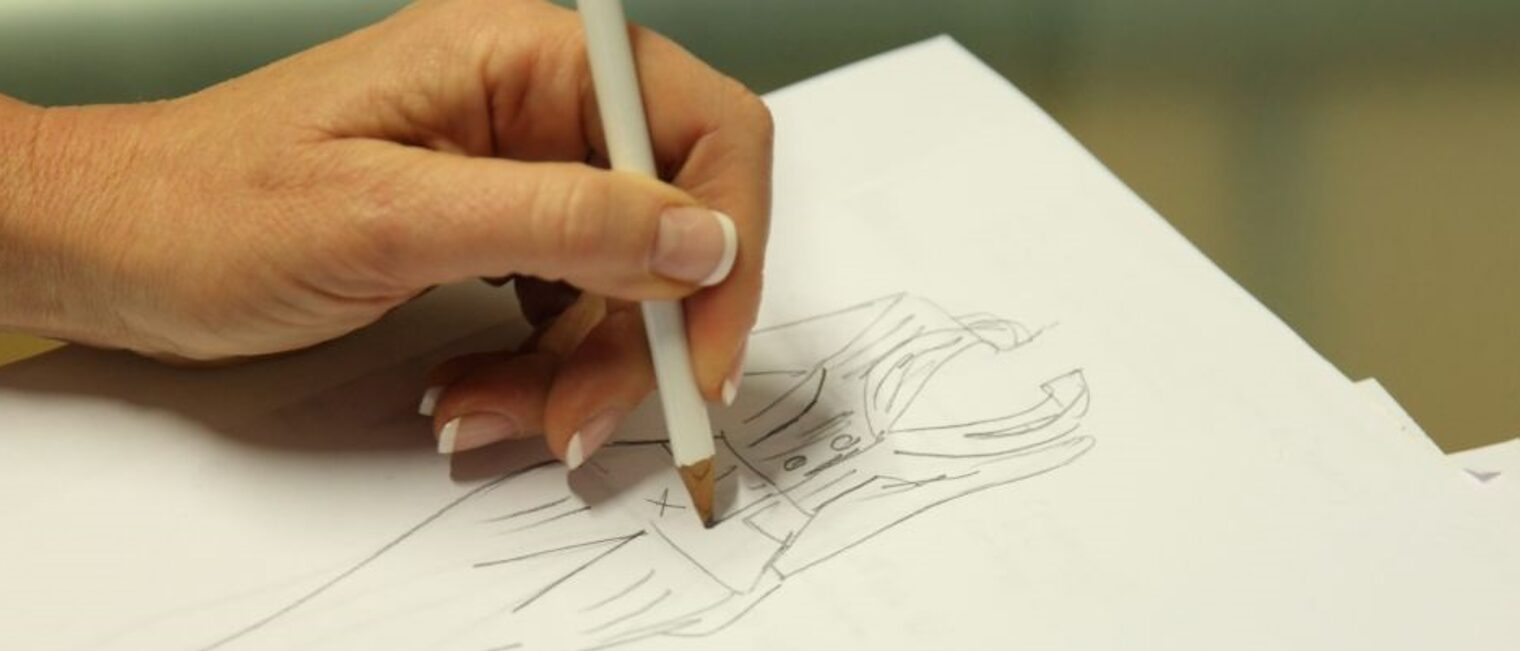 Eine Hand zeichnet eine Skizze eines Outfits auf ein Papier
