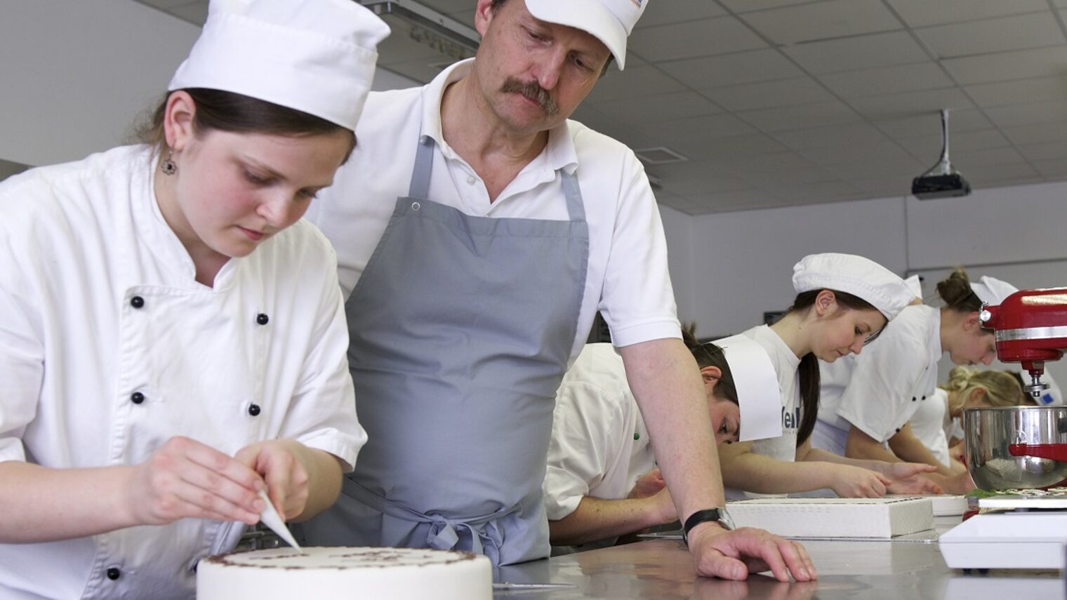 Bäckermeister schaut Schülerin bei der Arbeit zu