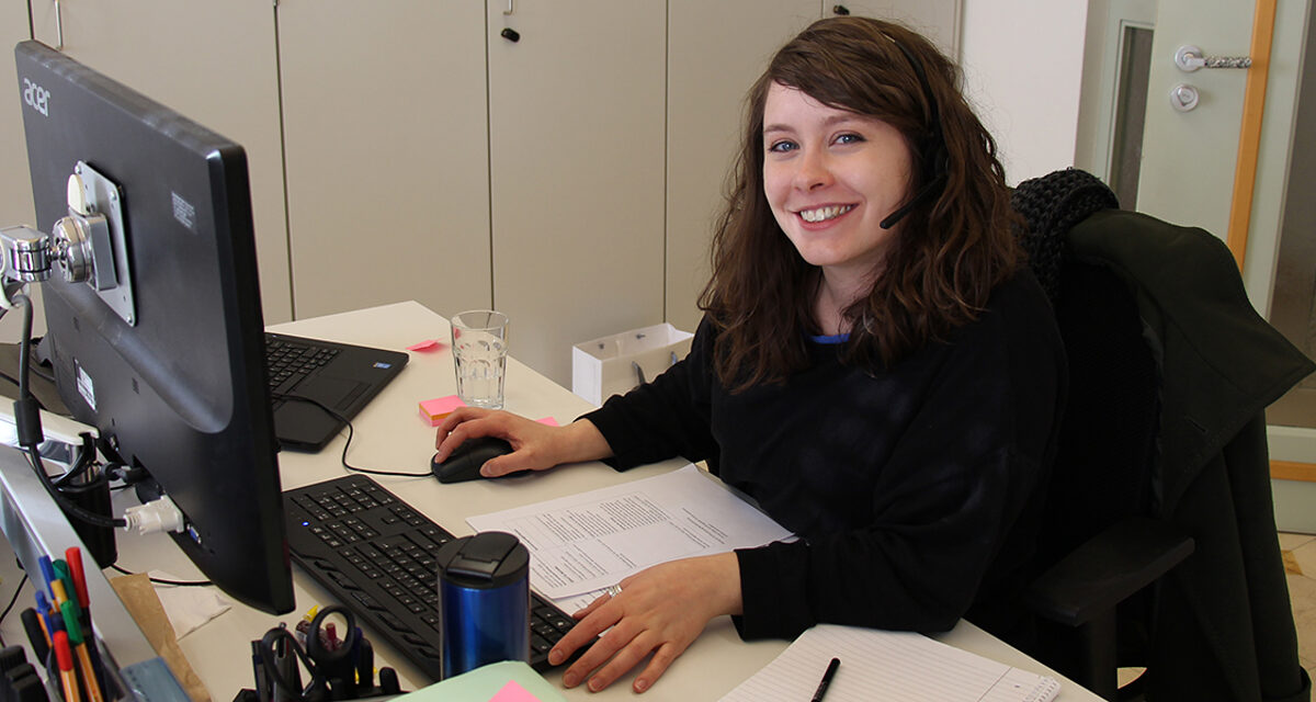Daniela Sabatino mit Headset am Schreibtisch vor Monitor.