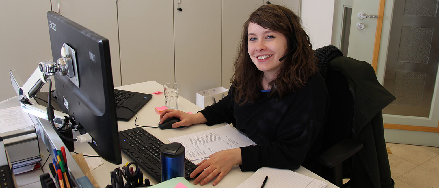 Daniela Sabatino mit Headset am Schreibtisch vor Monitor.