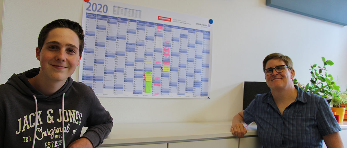 Aufgrund der Corona-Pandemie sind Azubis in besonderem Maße auf die Unterstützung ihrer Ausbilder angewiesen. Azubi und Ausbilderin im Büro vor Kalender.