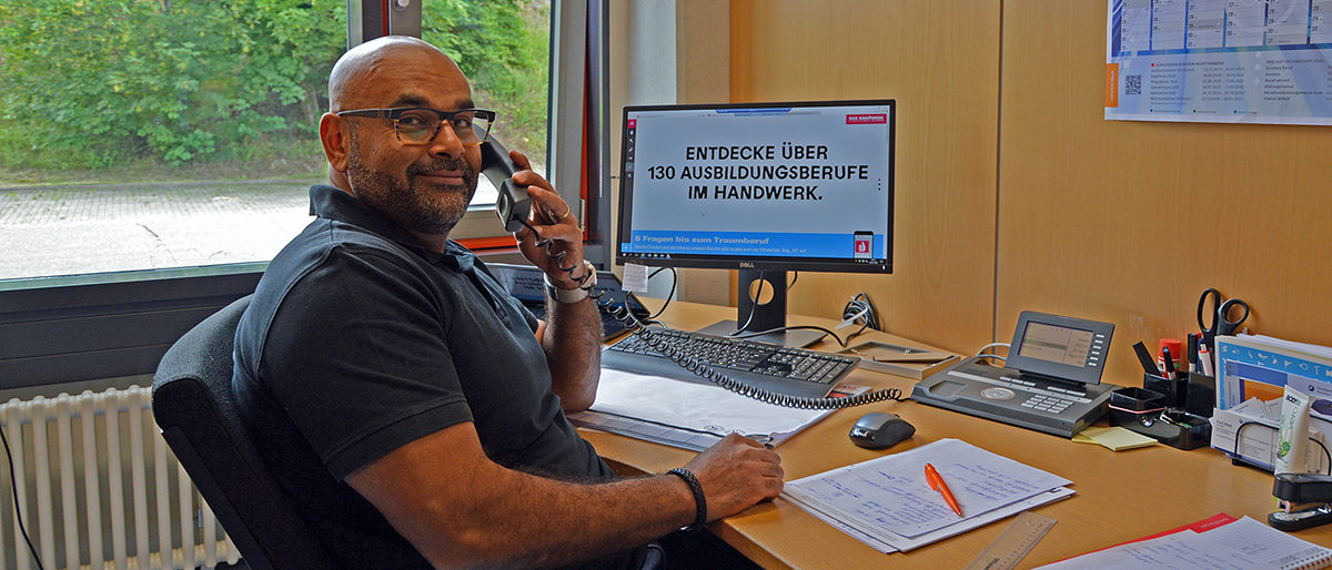 Baris Abak unterstützt Geflüchtete und Betriebe beim Start in die Ausbildung. Der Kümmerer Baris Abak am Schreibtisch mit Telefonhörer am Ohr.