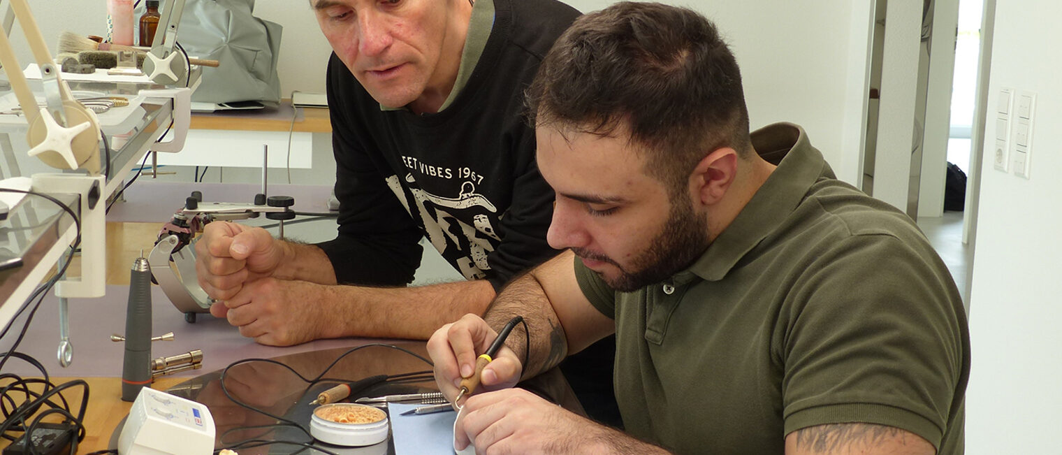 Zahntechnikermeister Markus Mayer (links) schaut Azubi Abdullah Touma beim Arbeiten über die Schulter.