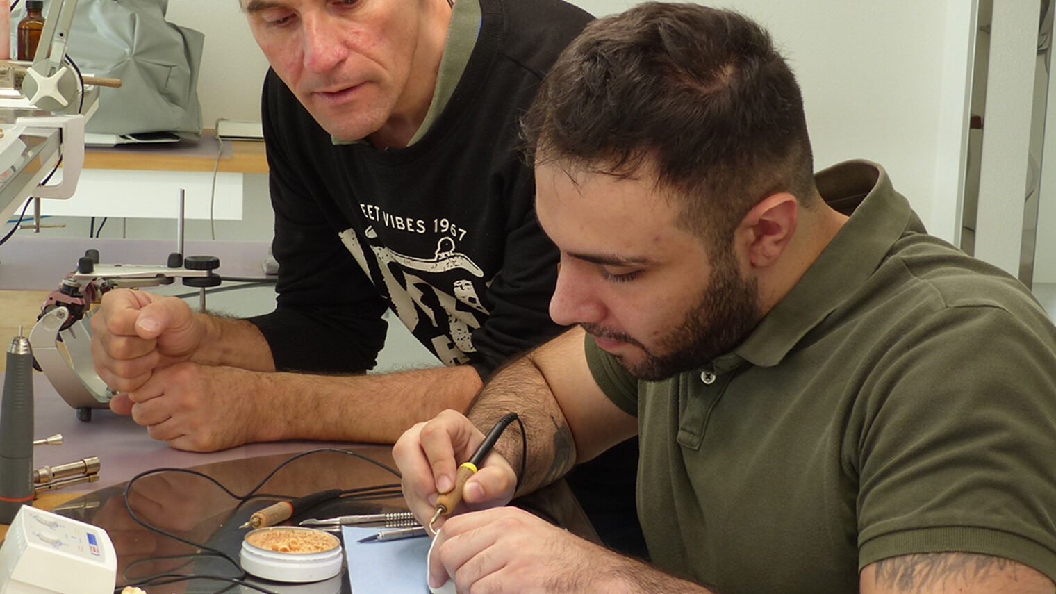 Zahntechnikermeister Markus Mayer (links) schaut Azubi Abdullah Touma beim Arbeiten über die Schulter.