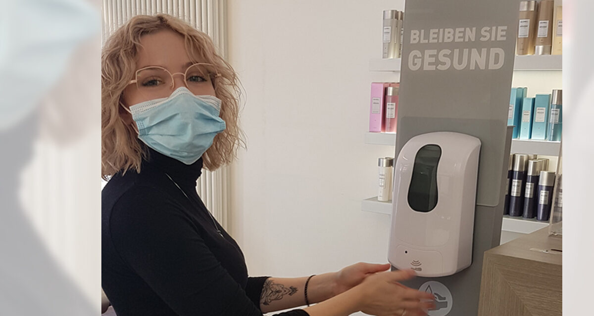 Julia Harzer mit Mundschutz betätigt Desinfektionsmittelspender in Friseursalon.