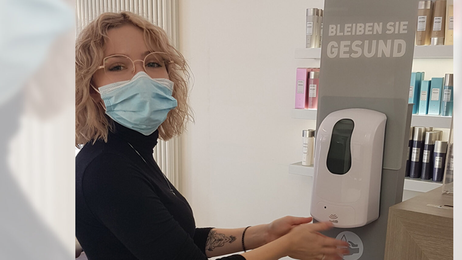 Julia Harzer mit Mundschutz betätigt Desinfektionsmittelspender in Friseursalon.