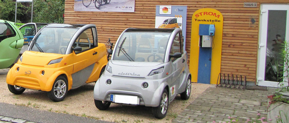 KfW-Zuschuss für die Einrichtung von Ladepunkten an Stellplätzen von Wohngebäuden. Elektroautos vor Stromtankstelle.