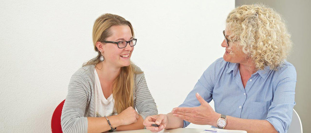 Alle Informationen zu Deiner Ausbildung im Handwerk. Ältere Frau erklärt einer jüngeren Frau etwas, beide sitzen an einem Tisch.