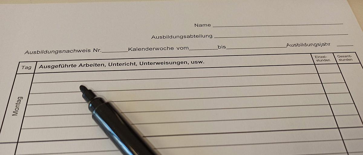 Berichtsheft erfolgreich führen. Geöffneter Stift liegt auf Berichtsheft.