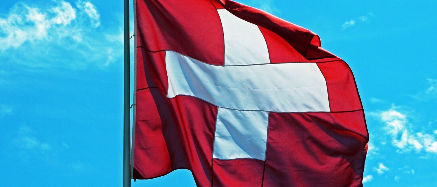 schweizer Flagge (weißes Kreuz vor rotem Grund) vor Himmel
