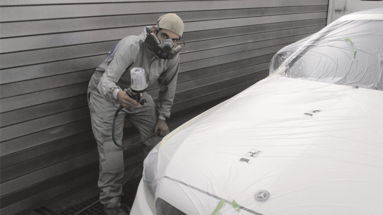Autolackierer in Lackierkabine bei der Arbeit.