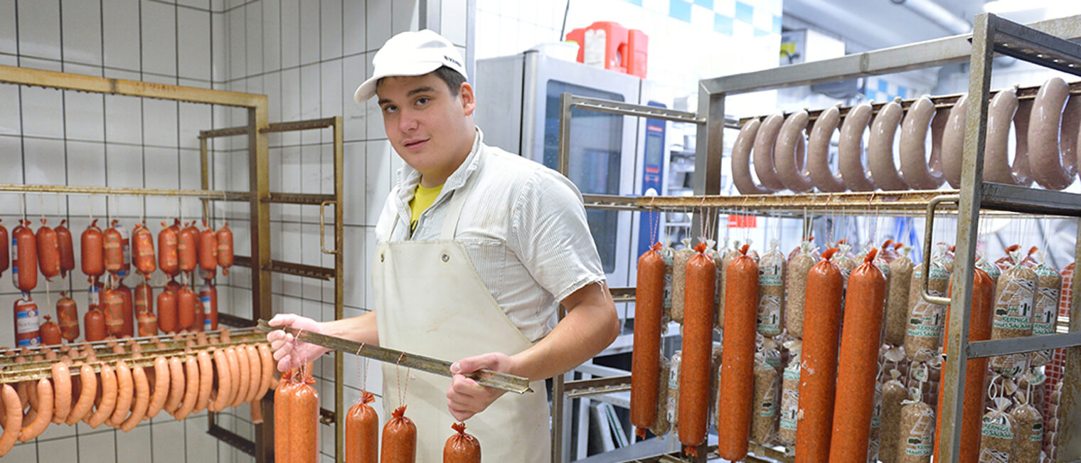 Metzger hält eine Stange mit Würsten in der Hand, Metzgerei Braun in Wiedenzhausen.