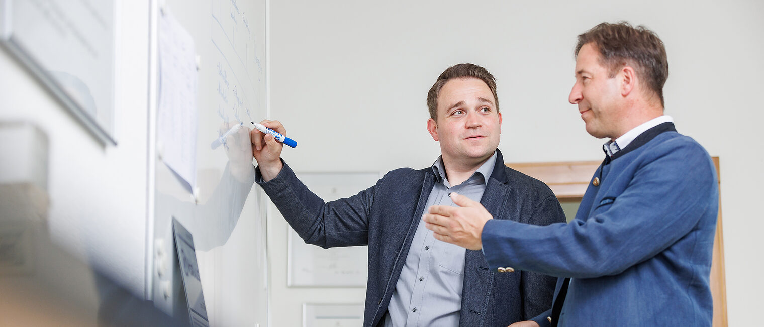 Dennis Schäuble und Lothar Hempel vom Unternehmensservice der Handwerkskammer Konstanz stehen mit Stift in der Hand vor einem Whiteboard.