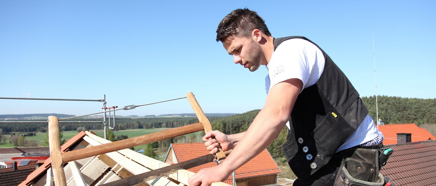 Mann auf Dach sägt Holzbalken durch