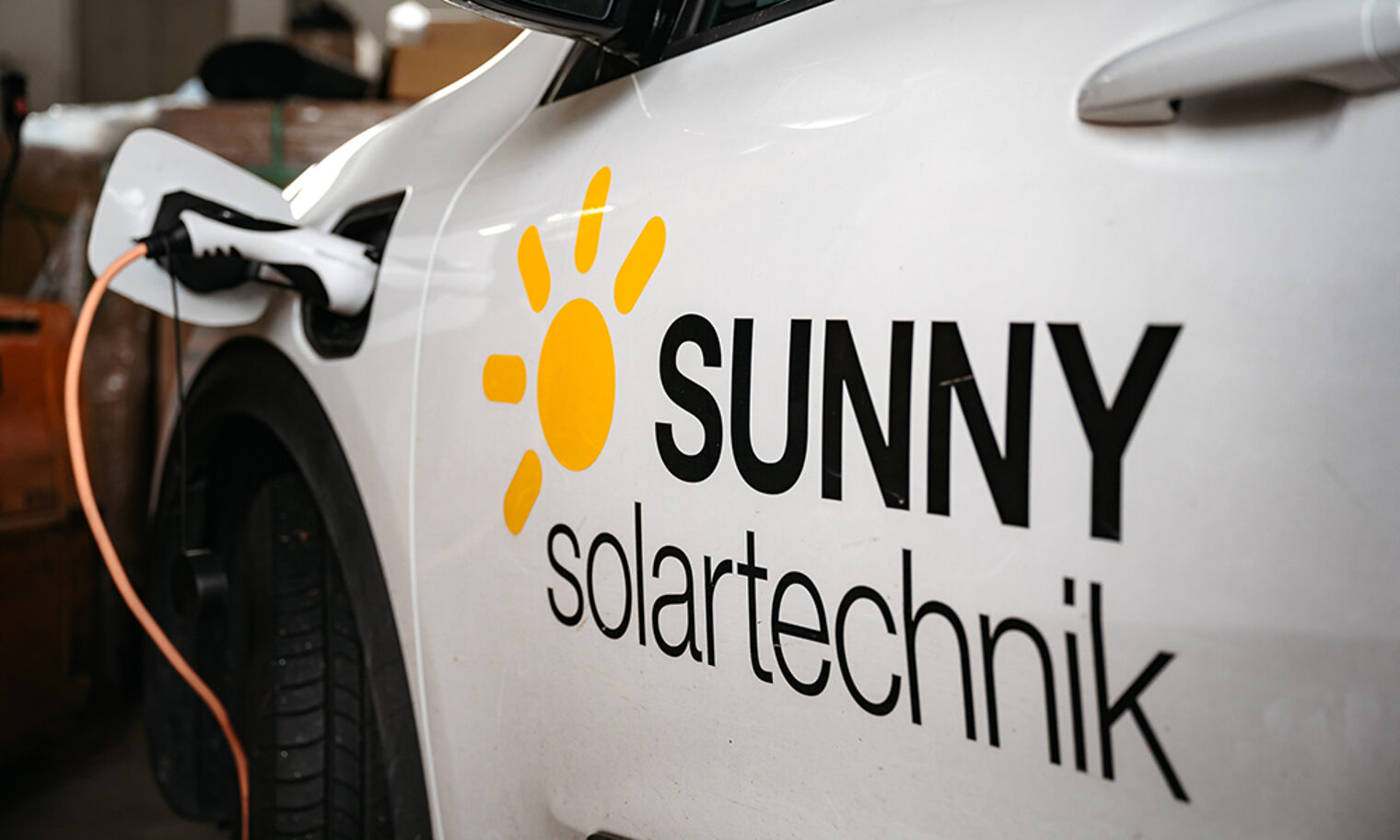 Detailansicht von E-Auto beim Laden. Aufschrift Sunny Solartechnik