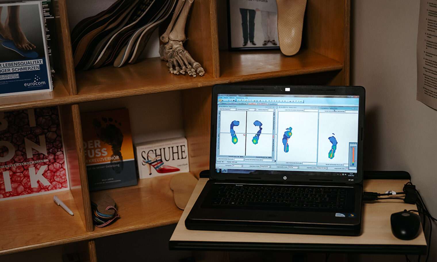 Aufgeklapptes Laptop zeigt Abbildungen von Fußsohlen in einer Schuhmacher-Werkstatt.