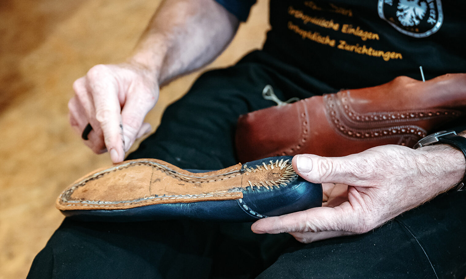 Schuhmacher deutet auf die Naht eines zu reparierenden Schuhs.