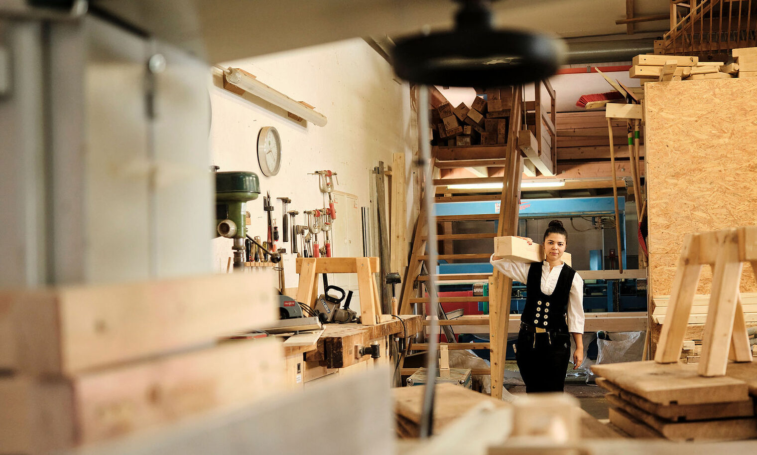 Junge Zimmerin mit Holzbalken auf der Schulter in Werkstatt,