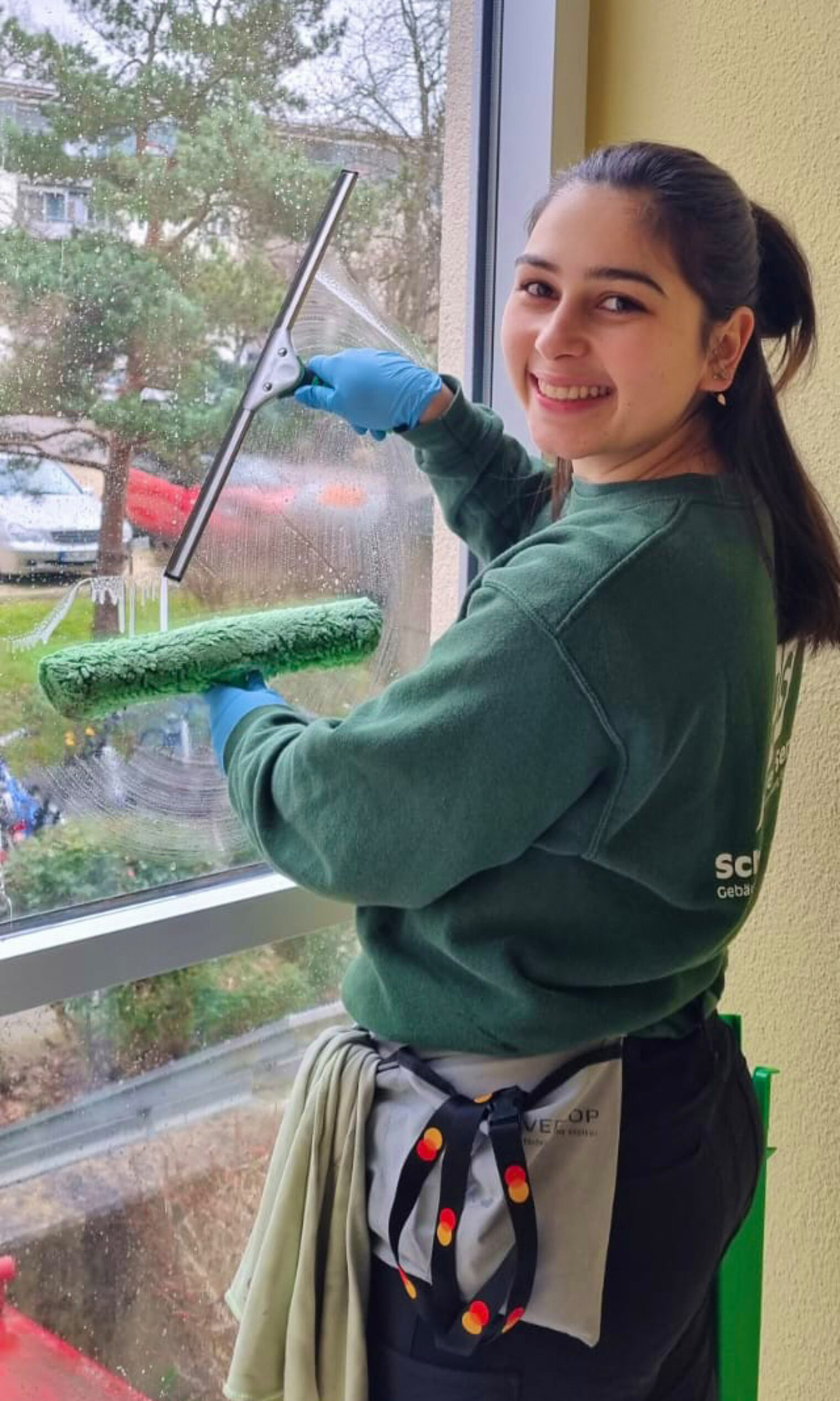 Gebäudereinigerin Sarah Lutz putzt ein Fenster und lächelt in die Kamera.