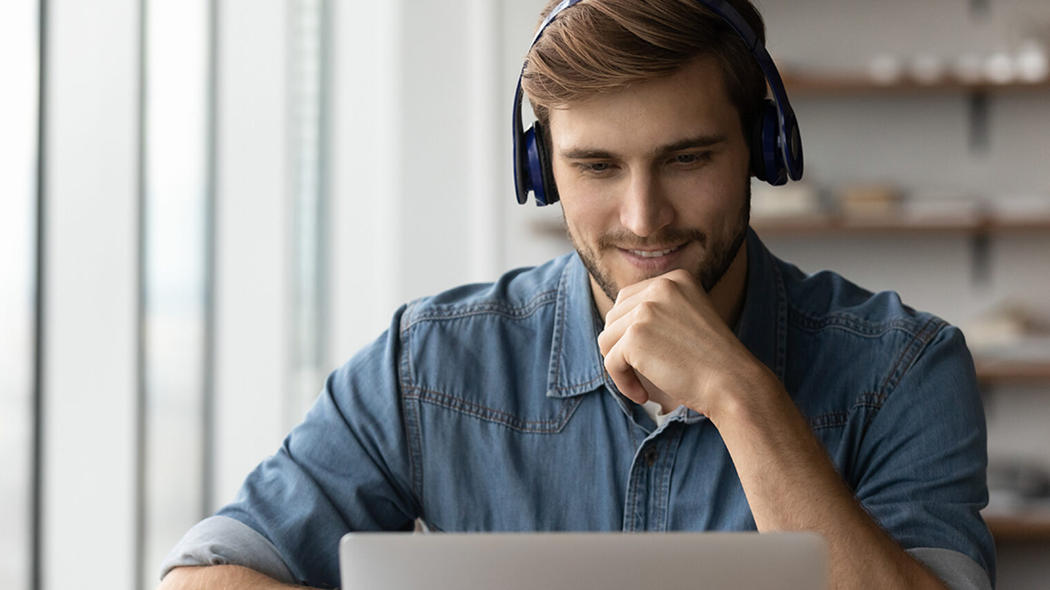 Junger Mann mit Headset schaut in Laptop-Bildschirm.