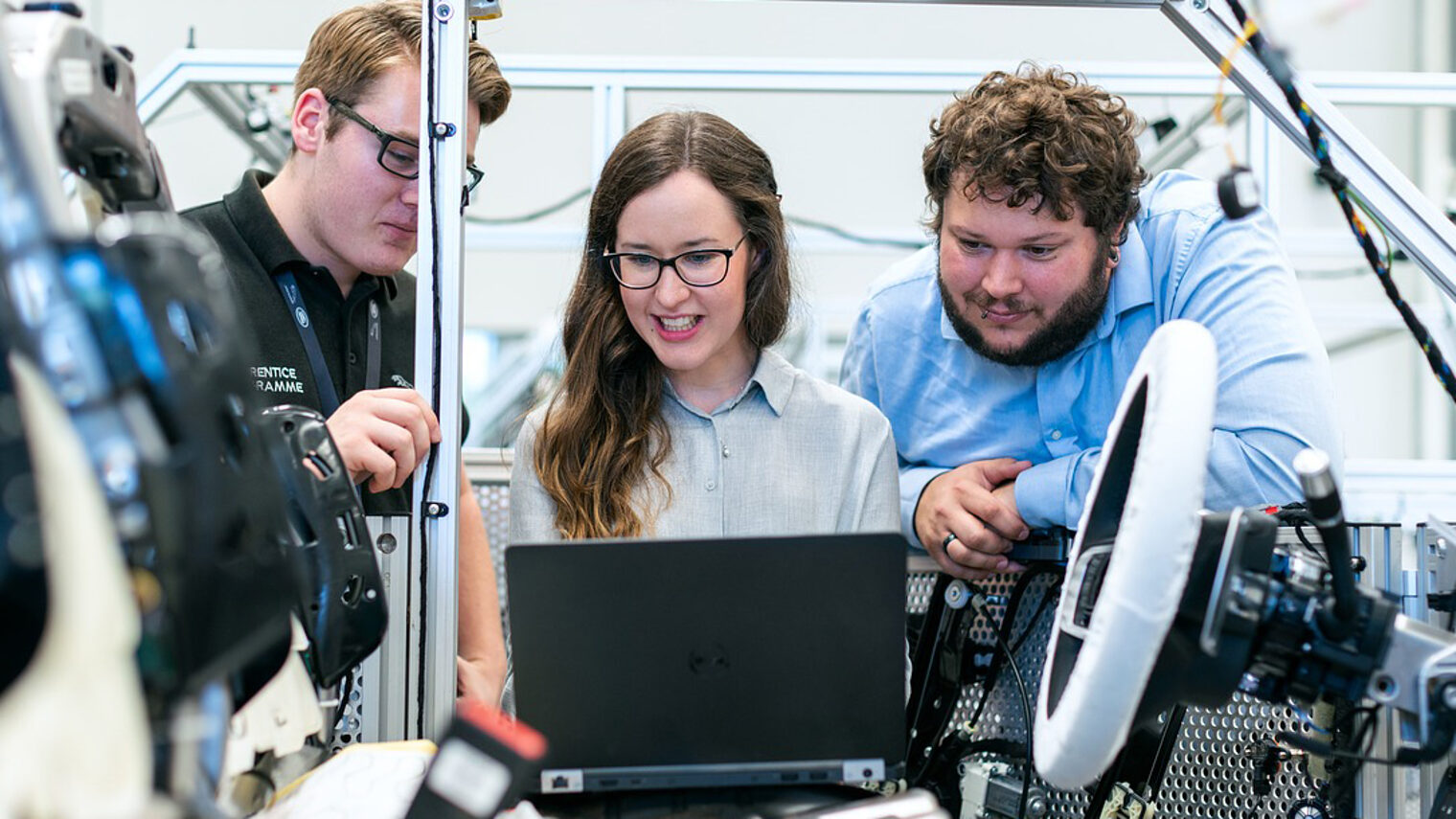 Drei junge Menschen vor Laptop in Werkstatt.