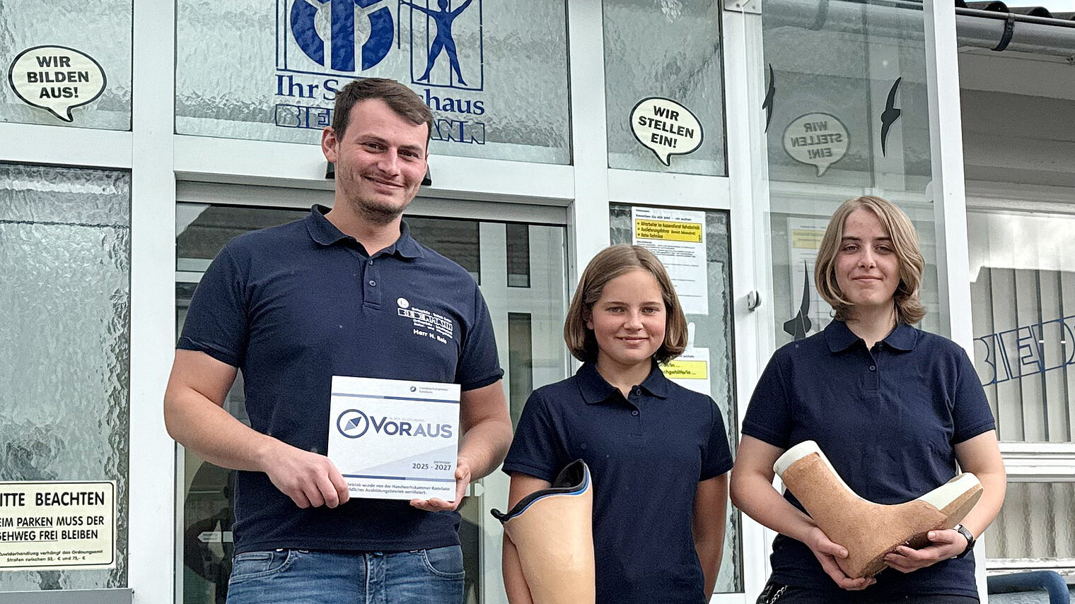 Nils Reis von Biedermann Orthopädie-Technik mit seinen Auszubildenden Selina Preuss und Stefanie Kopp, die Bein-Prothesen in den Händen halten.