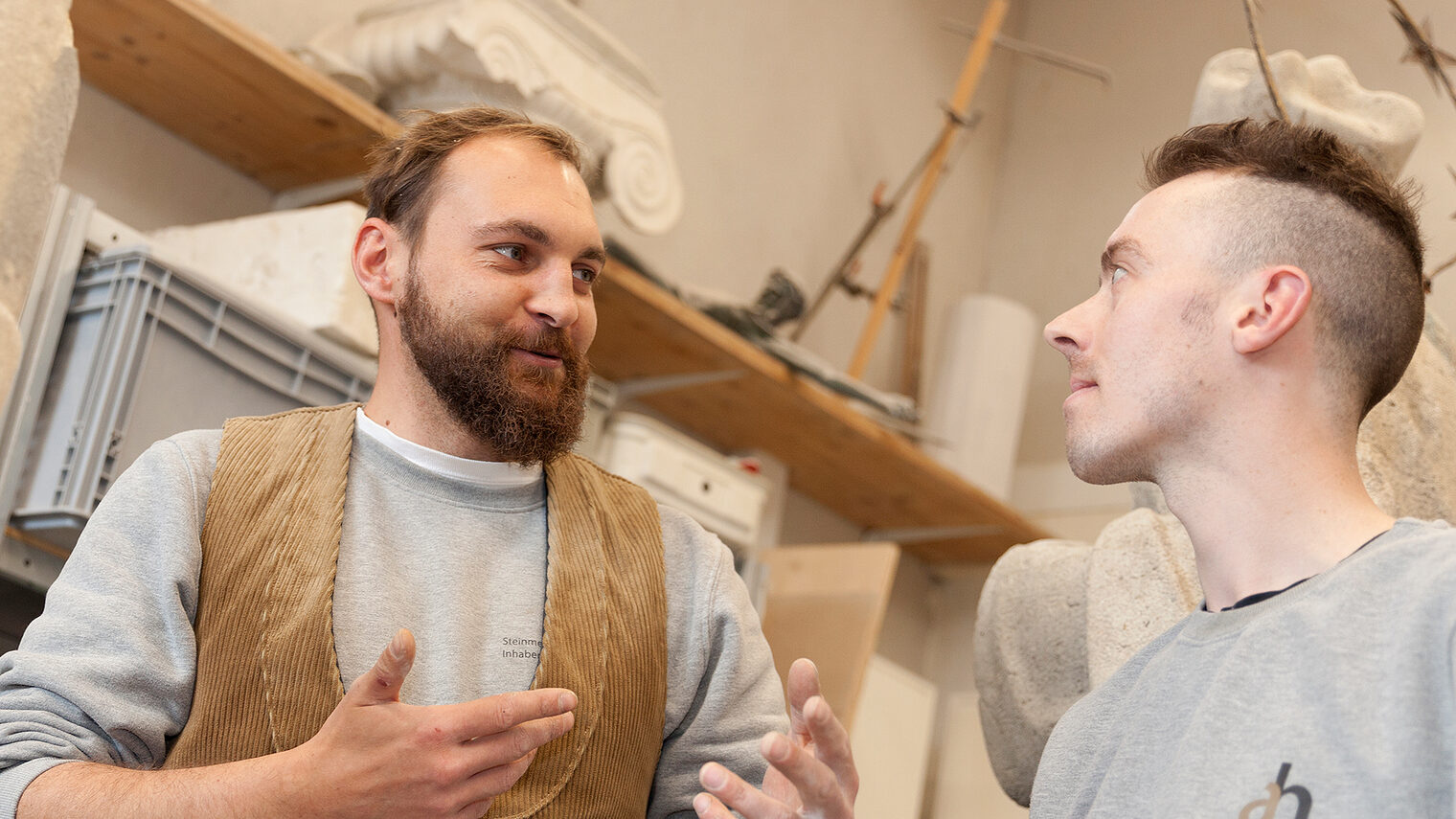 Steinmetz unterhält sich mit jungem Mitarbeiter in der Werkstatt.