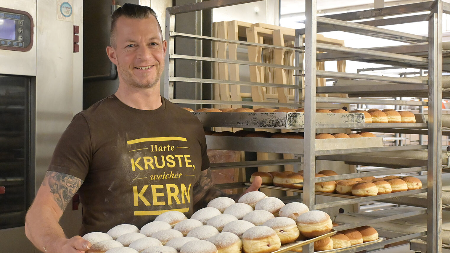 Bäckermeister Manuel Beha präsentiert in seiner Backstube ein Blech mit frisch gebackenen Berlinern.