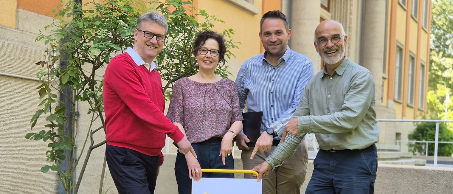 Innovationspreis Junges Handwerk Vier Personen hinter einem gelben Stuhl weisen mit ihren Händen auf ein Schild zum Innovationspreis