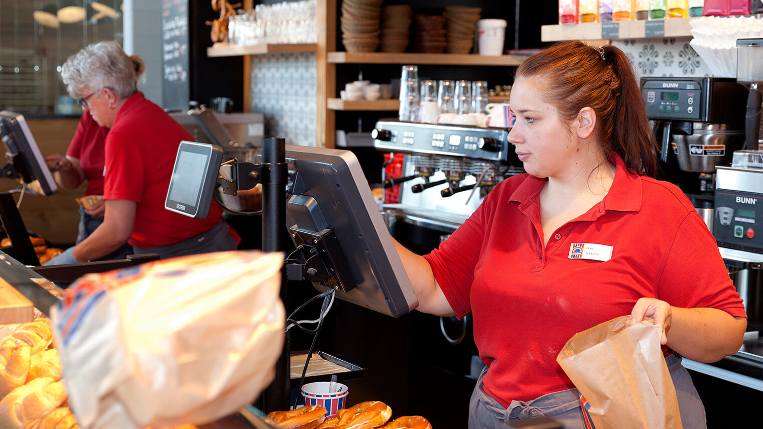Junge Verkäuferin hinter der Theke in einer Bäckerei tippt etwas in die Kasse ein.