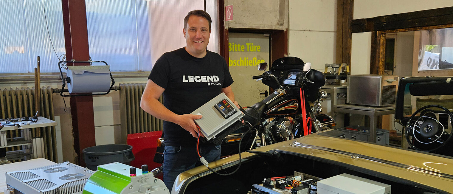Clemens Hummel vor Motor eines Oldtimers mit elektronischer Steuereinheit in der Hand.