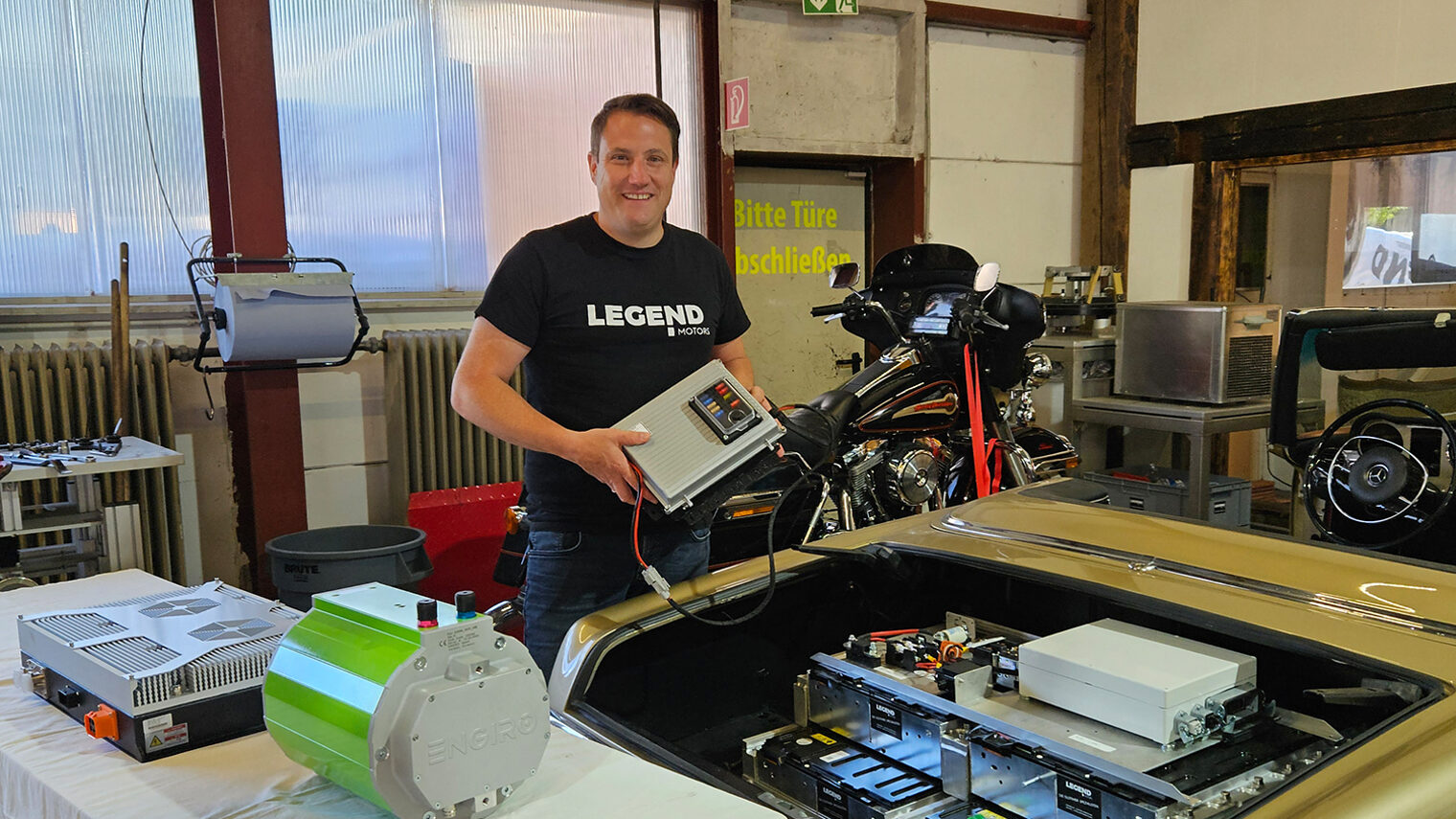 Clemens Hummel vor Motor eines Oldtimers mit elektronischer Steuereinheit in der Hand.
