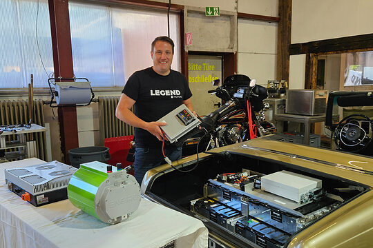 Clemens Hummel vor Motor eines Oldtimers mit elektronischer Steuereinheit in der Hand.