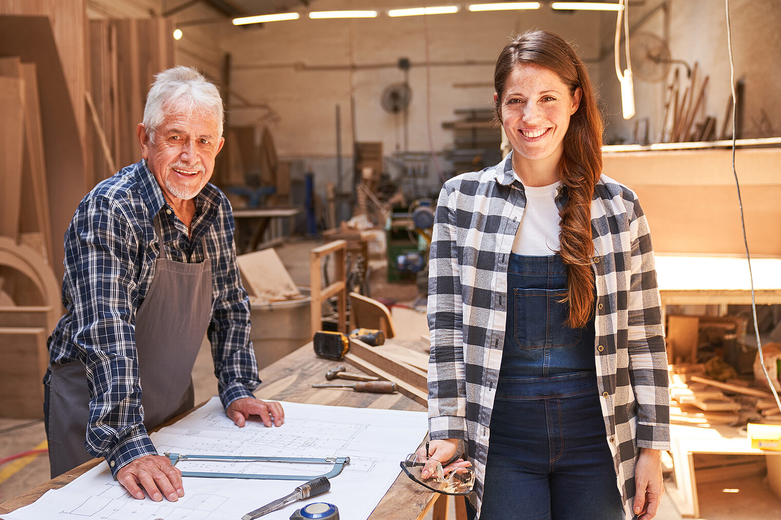 Älterer Schreiner und junge Schreinerin in einer Werkstatt.