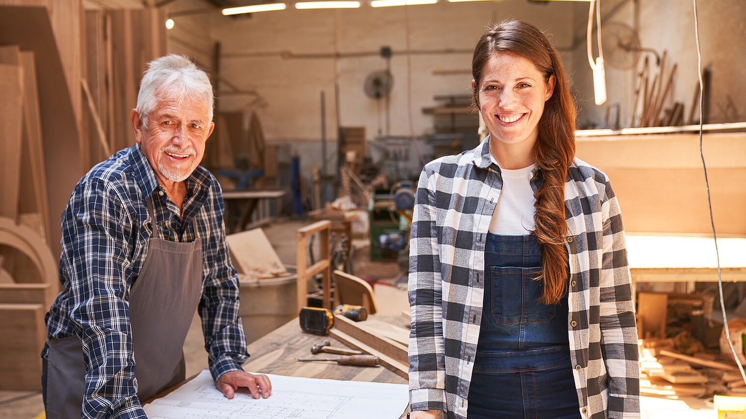 Älterer Schreiner und junge Schreinerin in einer Werkstatt.