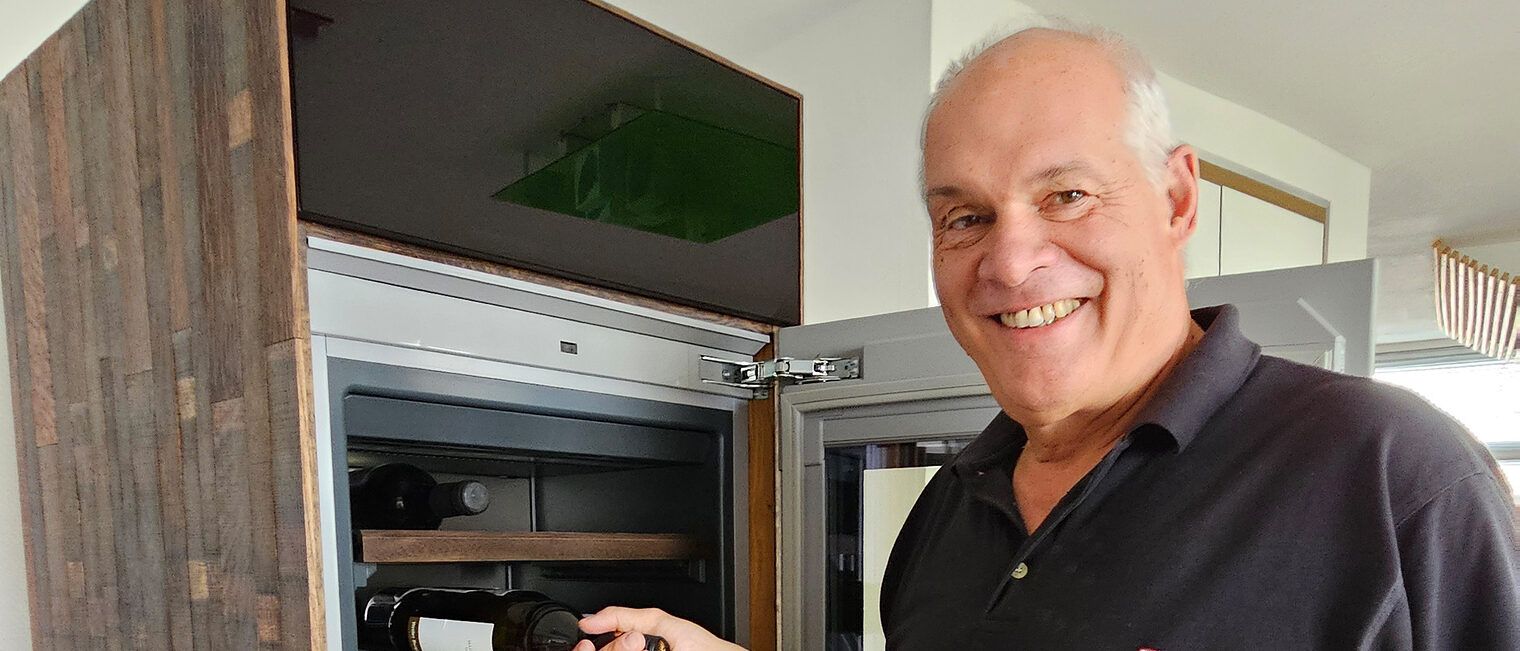 Schreinermeister Egon Kupferschmid legt eine Weinflasche in einen von ihm gebauten Weintemperierschrank aus einem alten Weinfass.