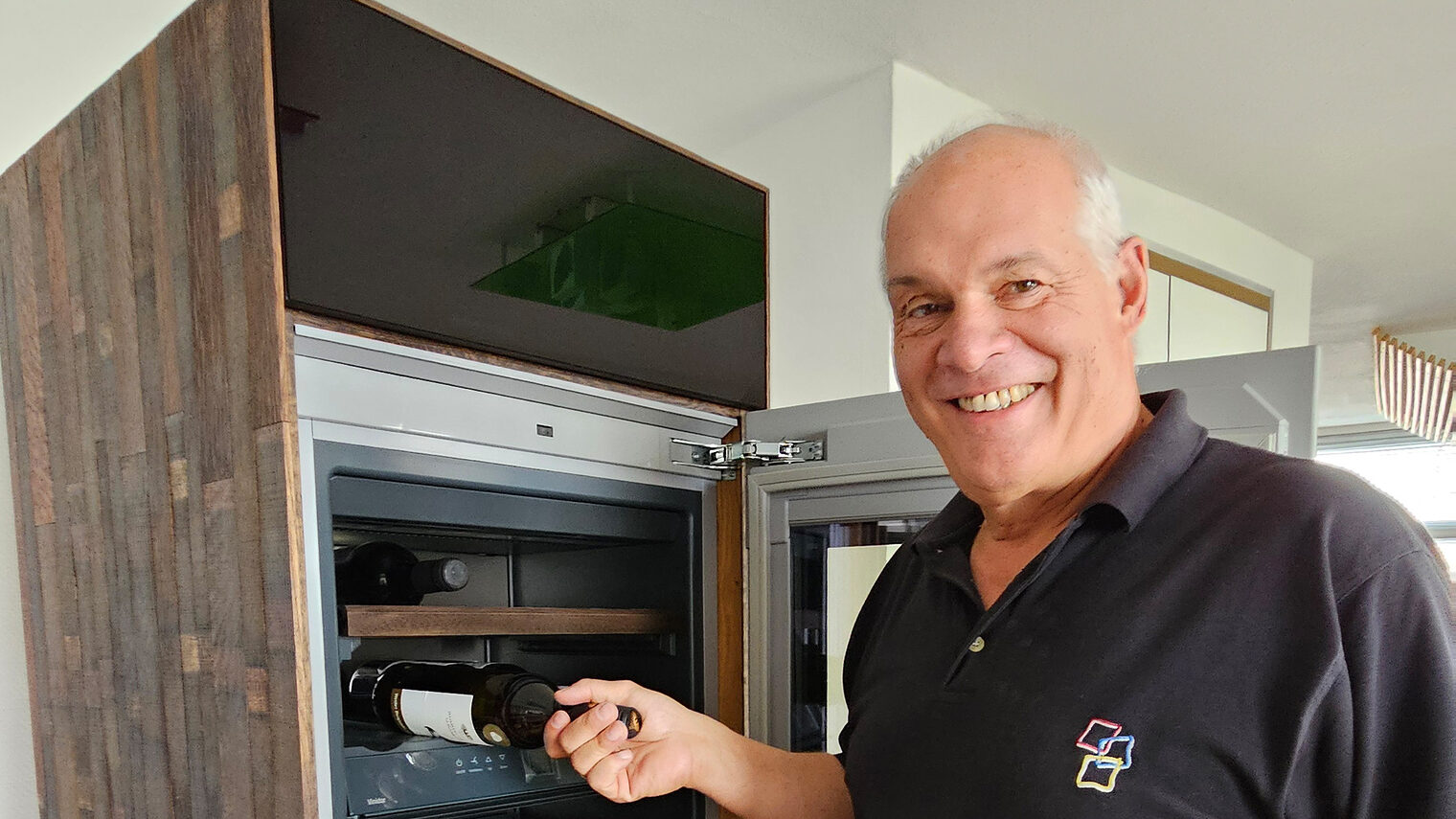 Schreinermeister Egon Kupferschmid legt eine Weinflasche in einen von ihm gebauten Weintemperierschrank aus einem alten Weinfass.