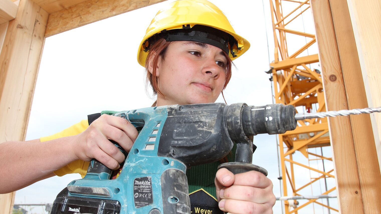 Junge Frau bohrt auf einer Baustelle in Holz.