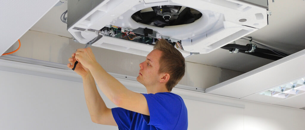 Junger Kältetechnik-Mechatroniker montiert eine Anlage an einer Decke.