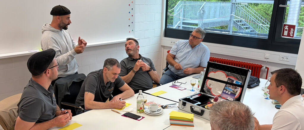 Sechs Männer, vor allem Lehrmeister an den Bildungsakademien der Handwerkskammer Konstanz, sitzen an einem Tisch und hören einem weiteren Mann zu, der zu ihnen spricht.