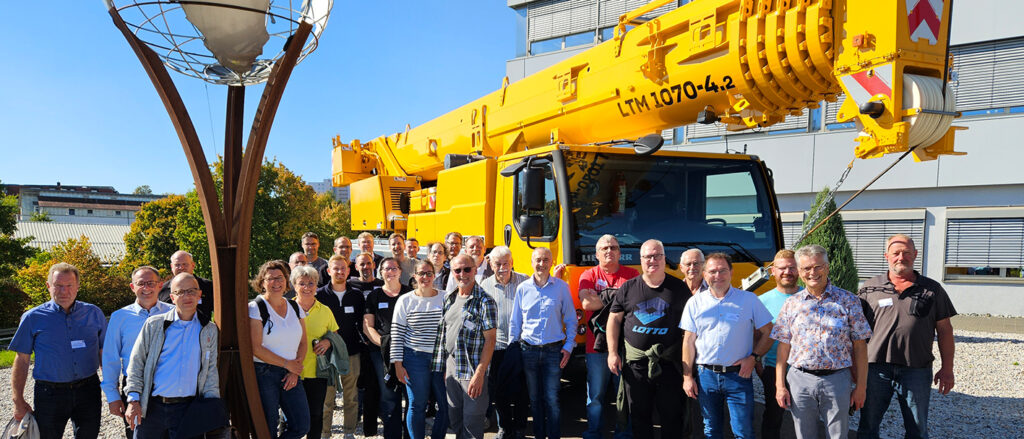 Gruppenbild der Exkursionsteilnehmer vor einem großen gelben Kran vor dem Liebherr-Werk in Ehingen.