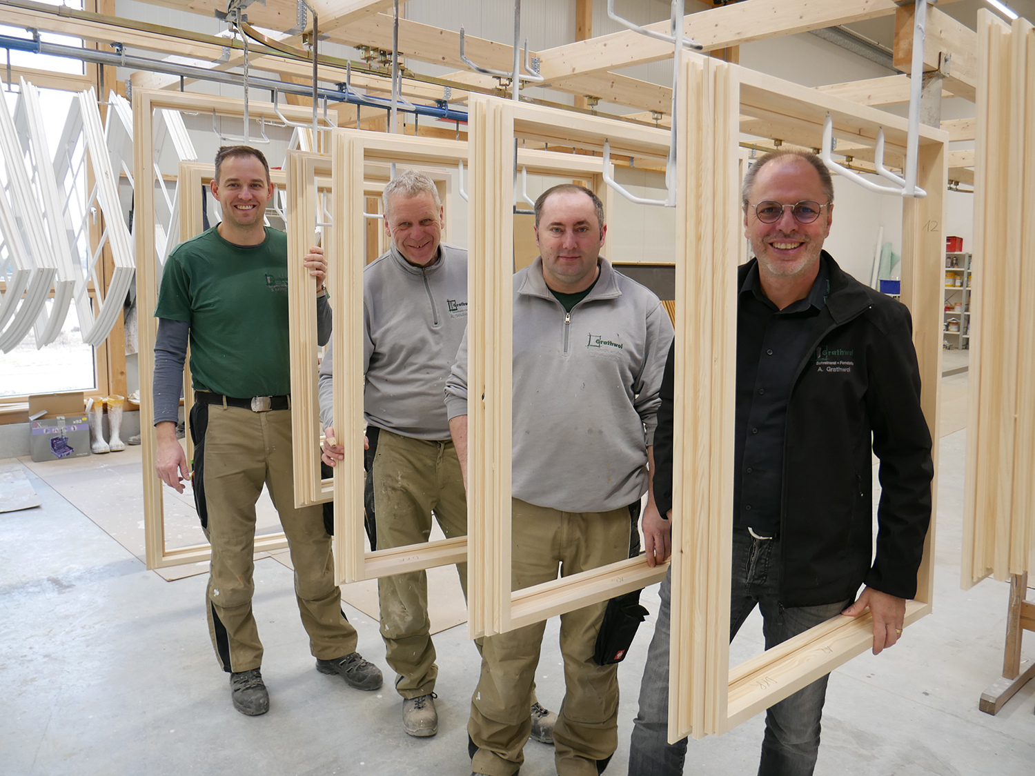Gruppenfoto: Mitarbeiter von Grathwol Fensterbau hintereinander aufgereiht zwischen Holz-Fensterrahmen.