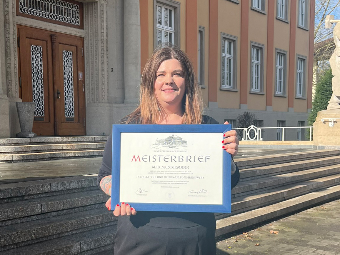 Rebecca Bürgi steht mit gerahmtem Meisterbrief in der Hand vor der Handwerkskammer Konstanz.