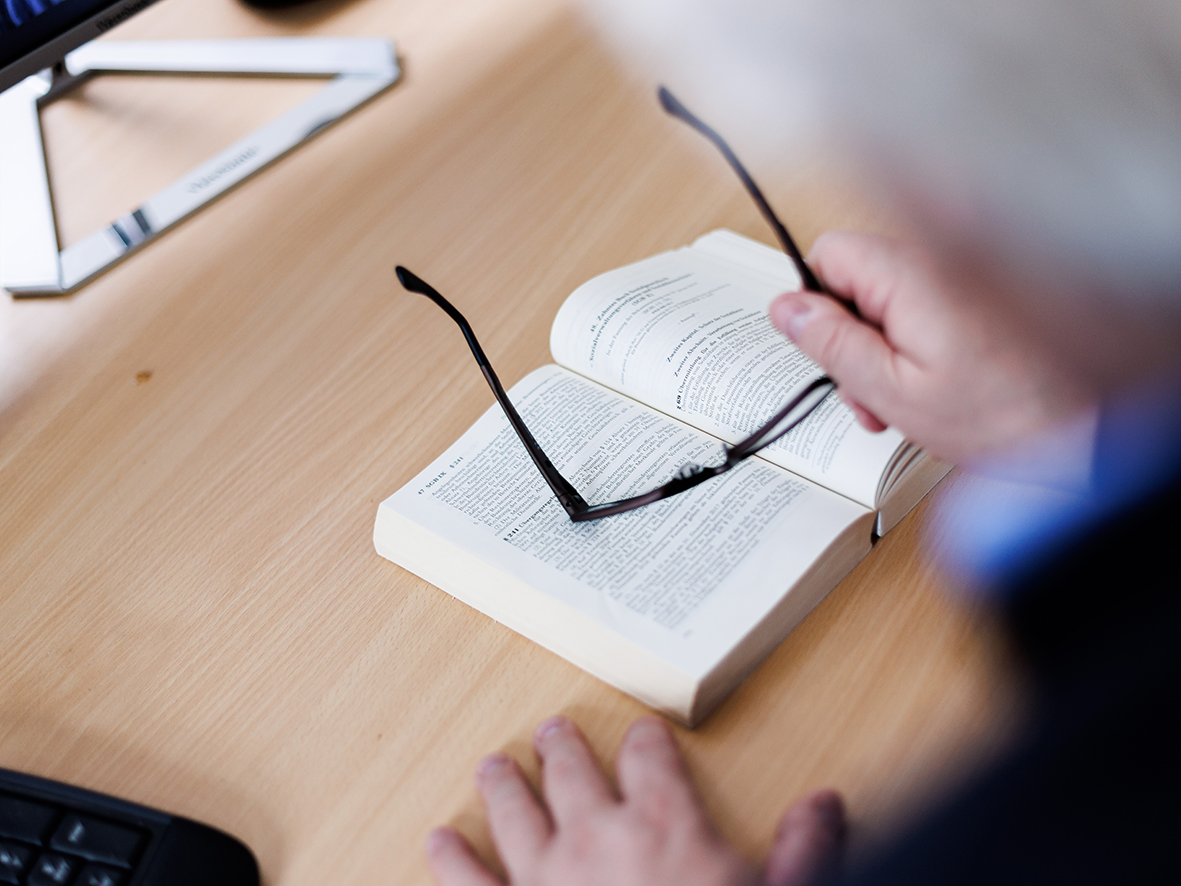 Rechtsberater Joachim Vojta beugt sich sich über ein aufgeschlagenes Buch, Brille in der rechten Hand.